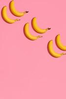 Pattern composition of a pair of bananas lying next to a pink background , top view photo