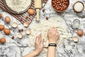 Close-up shot. Top view of a baker cook place, hands are working with a raw dough on the marble table background. photo