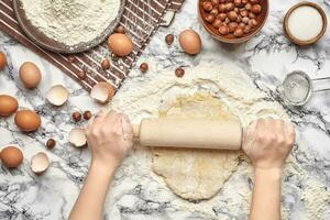 Close-up shot. Top view of a baker cook place, hands are working with a raw dough on the marble table background. photo