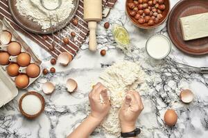 Close-up shot. Top view of a baker cook place, hands are working with a raw dough on the marble table background. photo