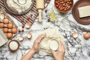 Close-up shot. Top view of a baker cook place, hands are working with a raw dough on the marble table background. photo