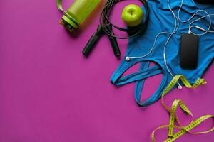 Health fitness background. Sneakers, dumbbell, power grip, green apple, water bottle, blue shirt, phone and earphone on dark background. photo