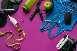 Health fitness background. Sneakers, dumbbell, power grip, green apple, water bottle, blue shirt, phone and earphone on dark background. photo