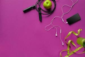 Health fitness background. Sneakers, dumbbell, power grip, green apple, water bottle, blue shirt, phone and earphone on dark background. photo