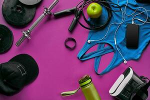 Health fitness background. Sneakers, dumbbell, power grip, green apple, water bottle, blue shirt, phone and earphone on dark background. photo