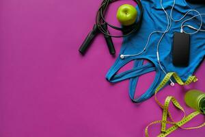 Health fitness background. Sneakers, dumbbell, power grip, green apple, water bottle, blue shirt, phone and earphone on dark background. photo