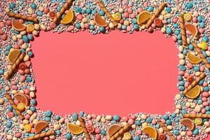 Multicolored glazed dragees and other sweets are arranged in the form of a frame on a coral background. photo