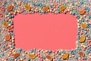 Multicolored glazed dragees and other sweets are arranged in the form of a frame on a coral background. photo