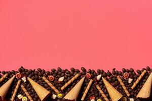 Chocolate dragee and waffle cones placed in fascinating order on coral background, view from above photo