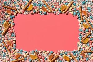 Multicolored glazed dragees and other sweets are arranged in the form of a frame on a coral background. photo