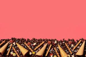 Chocolate dragee and waffle cones placed in fascinating order on coral background, view from above photo