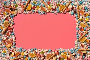 Multicolored glazed dragees and other sweets are arranged in the form of a frame on a coral background. photo