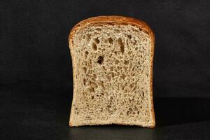 Half a loaf of fresh, tasty baked gray bread against black background with copy space. Close-up photo