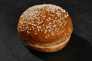 Fresh, yummy baked bun sprinkled with sesame seeds against black background with copy space. Rural cuisine or bakery. Close-up photo