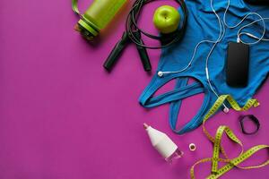 Health fitness background. Sneakers, dumbbell, power grip, green apple, water bottle, blue shirt, phone and earphone on dark background. photo