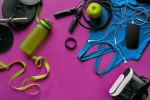 Health fitness background. Sneakers, dumbbell, power grip, green apple, water bottle, blue shirt, phone and earphone on dark background. photo