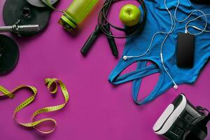 Health fitness background. Sneakers, dumbbell, power grip, green apple, water bottle, blue shirt, phone and earphone on dark background. photo