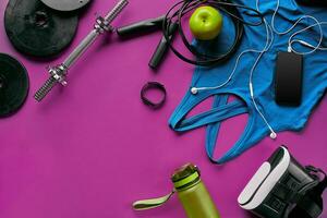 Health fitness background. Sneakers, dumbbell, power grip, green apple, water bottle, blue shirt, phone and earphone on dark background. photo