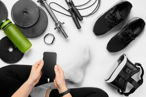 Young woman with mobile phone and sport equipment on white background flat lay top view. Fitness concept photo