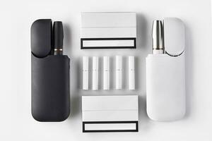 Black and white electronic cigarettes in open batteries, two packs, five heatsticks isolated on white. Hi-tech heating tobacco system. Close up photo