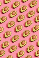 Colorful fruit pattern of fresh cutted avocado halves with pits on coral pink background, top view photo