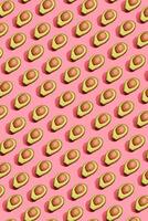 Colorful fruit pattern of fresh cutted avocado halves with pits on coral pink background, top view photo