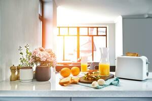 White electric bread toaster with orange juice with sandwich on kitchen table. Breakfast in the cozy kitchen. Sun flare photo