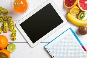 Fresh juice in glass from citrus fruits - lemon, grapefruit, orange, notebook with pencil on white wooden background photo