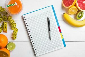 Fresh juice in glass from citrus fruits - lemon, grapefruit, orange, notebook with pencil on white wooden background photo