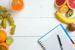 Fresh fruits with tape measure over white wooden background. Top view photo