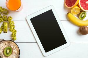 Fresh juice in glass from citrus fruits - lemon, grapefruit, orange, tablet on white wooden background photo