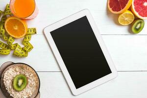 Fresh juice in glass from citrus fruits - lemon, grapefruit, orange, tablet on white wooden background photo