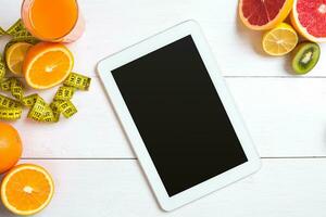 Fresh juice in glass from citrus fruits - lemon, grapefruit, orange, tablet on white wooden background photo