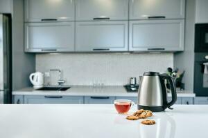 Breakfast scene at sunny morning. Transparent black tea mug with biscuit on kitchen table photo