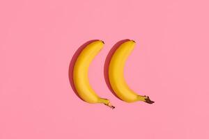 Composition of a pair of bananas lying next to a pink background in the center of the image, top view photo
