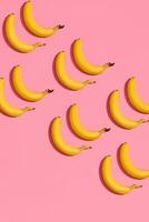 Pattern composition of a pair of bananas lying next to a pink background , top view photo