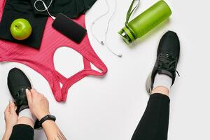 joven mujer en deportivo polainas cordones zapatillas, preparando para capacitación. accesorios para Deportes en blanco antecedentes plano laico parte superior vista. foto