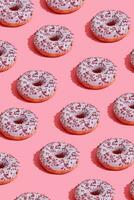 Food design with tasty pink glazed donut on coral pink pastel background top view pattern photo