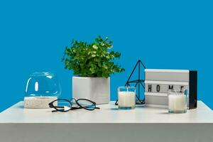 White table with candles on it and in a glass candlestick, greenery in pot, glasses, iron triangle, home decor element. Blue background. Close up photo