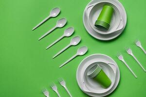 Colorful plastic disposable tableware on green background with copy space. The concept of picnic utensil. Top view. Selective focus. Close-up. photo