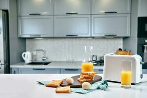 Toaster with fresh toast, eggs and glass of orange juice on a light kitchen table photo