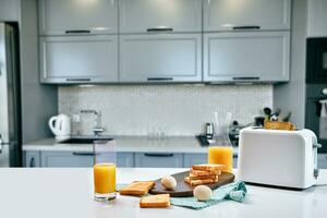 Toaster with fresh toast, eggs and glass of orange juice on a light kitchen table photo