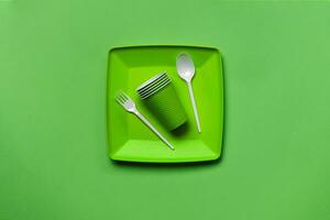 vistoso el plastico desechable vajilla en verde antecedentes con Copiar espacio. el concepto de picnic utensilio. parte superior vista. selectivo enfocar. de cerca. foto