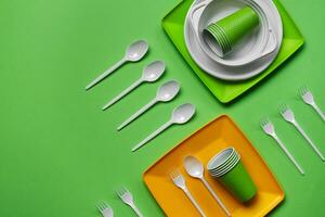 Colorful plastic disposable tableware on green background with copy space. The concept of picnic utensil. Top view. Selective focus. Close-up. photo