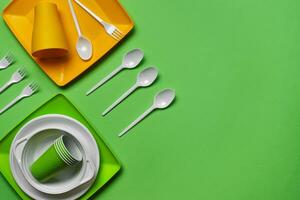 Colorful plastic disposable tableware on green background with copy space. The concept of picnic utensil. Top view. Selective focus. Close-up. photo