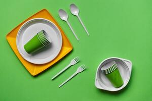 Colorful plastic disposable tableware on green background with copy space. The concept of picnic utensil. Top view. Selective focus. Close-up. photo