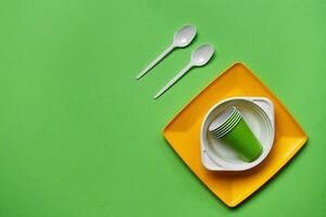 Colorful plastic disposable tableware on green background with copy space. The concept of picnic utensil. Top view. Selective focus. Close-up. photo