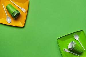 Colorful plastic disposable tableware on green background with copy space. The concept of picnic utensil. Top view. Selective focus. Close-up. photo