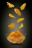 Grooved potato crisps falling down in glass bowl against a black background with copy space for text, images. Crispy chips. Advertising. Close-up. photo