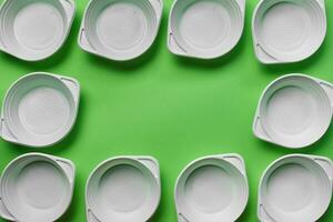 White plastic disposable tableware on green background with copy space. The concept of picnic utensil. Top view. Selective focus. Close-up. photo